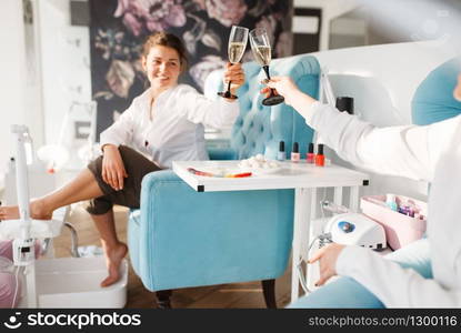 Two women with champagne in beauty salon. Professional beautician service, female customers, toenail and fingernail care in spa studio. Two women with champagne in beauty salon