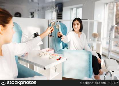 Two women with champagne in beauty salon. Professional beautician service, female customers, toenail and fingernail care in spa studio