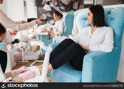 Two women with champagne, pedicure procedure in beauty salon. Professional beauticians and female customers, toenail care in spa studio