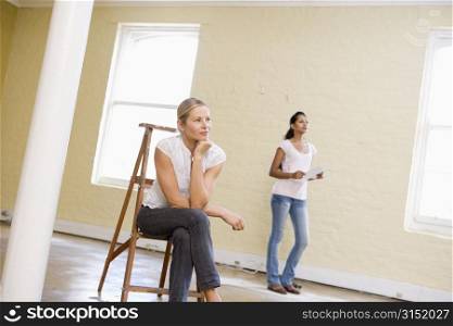 Two women with ladder in empty space holding paper