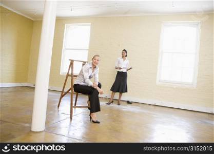 Two women with ladder in empty space holding paper smiling