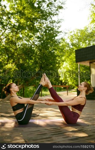 Two women with slim body doing exercise together on group yoga training in sunny day in park. Meditation, fit class on workout outdoors, relaxation practice. Fitness, active healthy lifestyle. Two women doing exercise together, yoga training