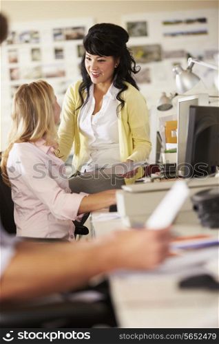 Two Women Working At Desks In Busy Creative Office