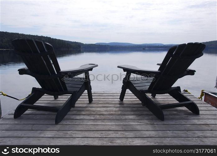 Two wooden adirondack chairs on a boat dock on a beautiful lake in the evening
