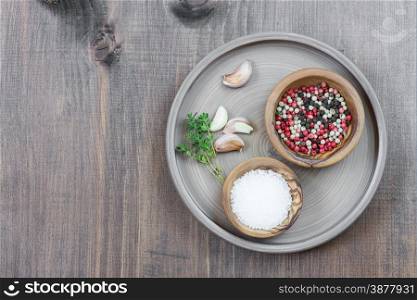 Two wooden bowls with salt and multicolored pepper and thyme sprigs in a ceramic plate on a wooden board with space for text