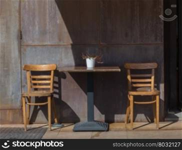 Two wooden chairs and a table against an interesting rusty wall.
