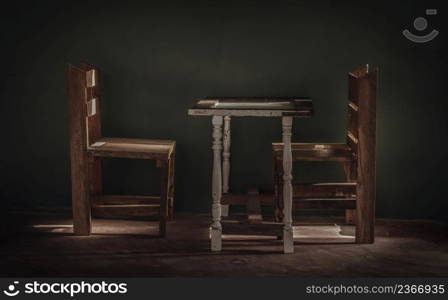 Two wooden chairs and old wooden white table standing front of green cement wall at an empty room through which a ray of light passes. Dark tone, Space for text, Selective focus.
