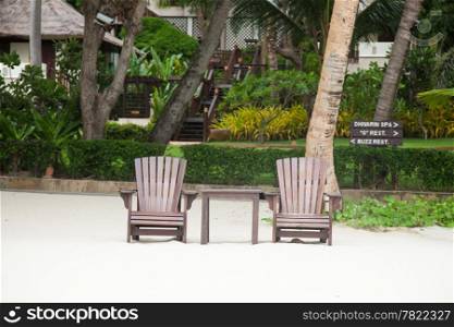 Two wooden chairs. On the beach. For on Koh Samet. Under coconut trees.