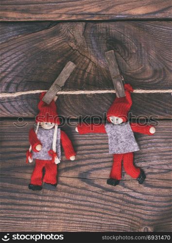 two wooden dolls hang on a rope, brown wooden background, vintage toning