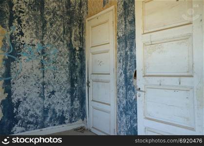 Two wooden doors and blue peeling wall with torn wallpaper in abandoned house.