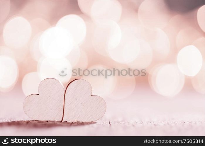Two wooden hearts on pink glowing bokeh hearts background for Valentines day. Two hearts on glitters