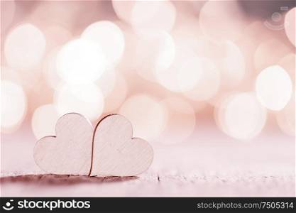 Two wooden hearts on pink glowing bokeh hearts background for Valentines day. Two hearts on glitters