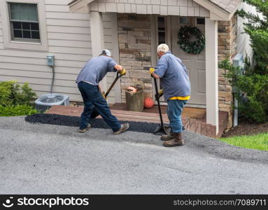 Two workers applying a layer of tarmac or extra blacktop onto asphalt street. Workers applying extra blacktop onto asphalt street
