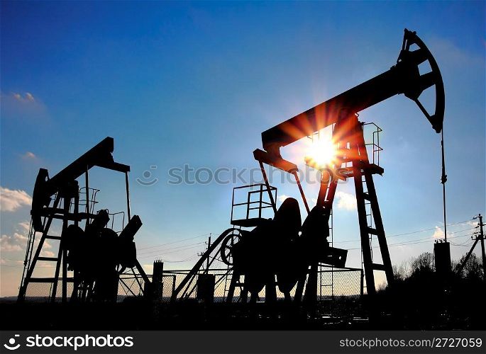 two working oil pumps silhouette against sun