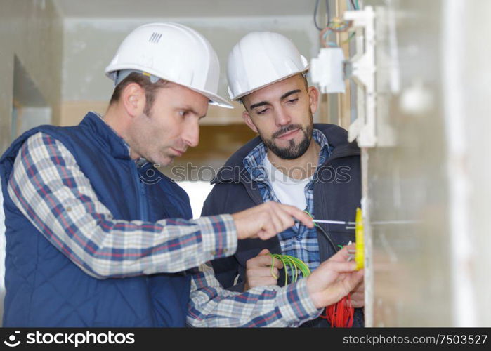 two workmen screwing electric terminal to wall