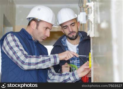 two workmen screwing electric terminal to wall