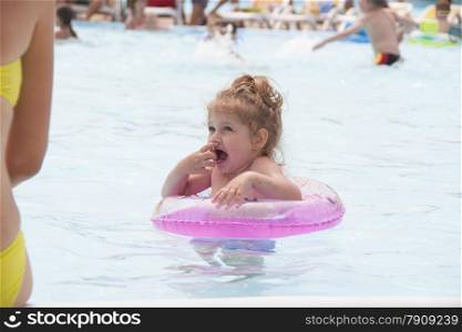 Two-year-old girl bathes in a public pool. Girl again entered the water and frozen from the cold water. Summer day.