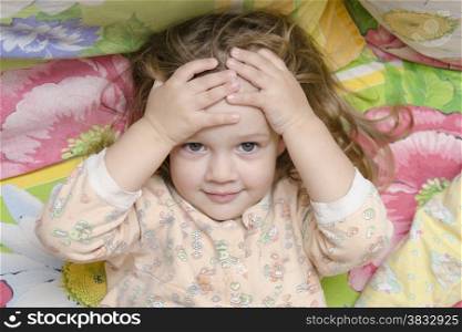 Two-year-old girl is in bed. The girl hugged his head in his hands and fun looking at the picture. Photo above. Portrait