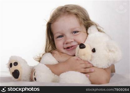 Two-year-old girl lies. Teddy bear sitting in front of her. Girl hugging a bear. Studio light background