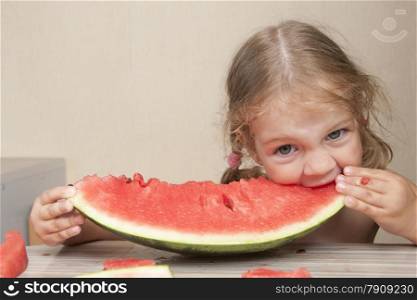 Two year old girl sitting at the kitchen table and eats with pleasure watermelon