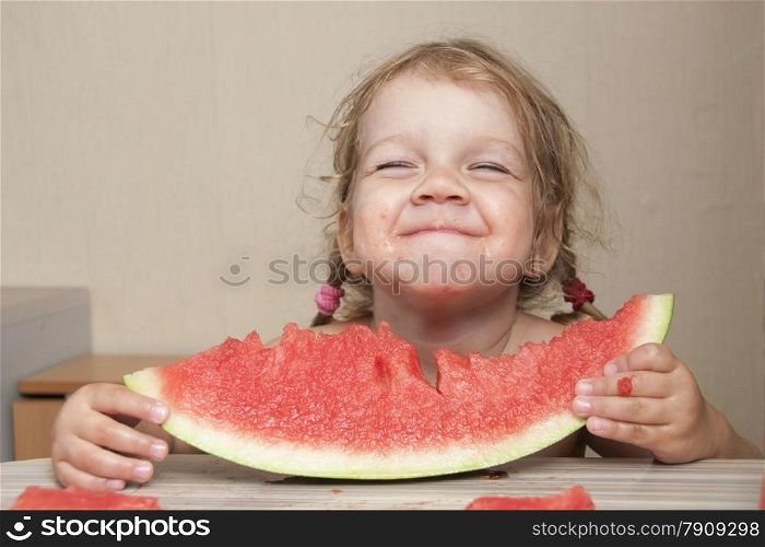 Two year old girl sitting at the kitchen table and eats with pleasure watermelon