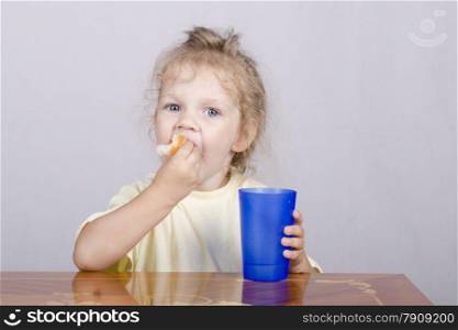 Two-year-old girl sitting at the table, eating a muffin and drinking from a plastic Cup