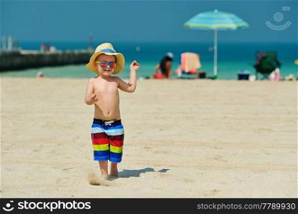 Two year old toddler boy in sun hat running on beach 
