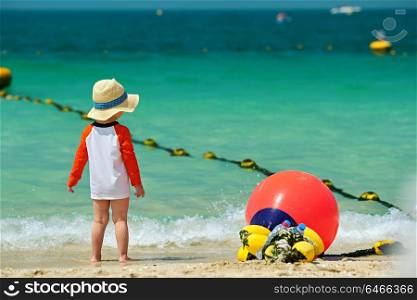 Two year old toddler boy in sun hat walking on beach