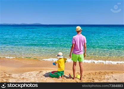 Two year old toddler boy on beach with father. Inflatable ring and beach toys. Summer family vacation. Sithonia, Greece. 