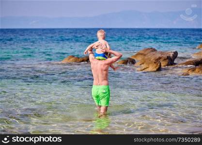 Two year old toddler boy on father’s shoulders at beach