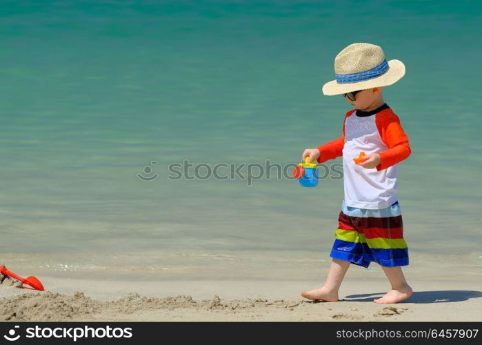 Two year old toddler boy playing with beach toys on beach