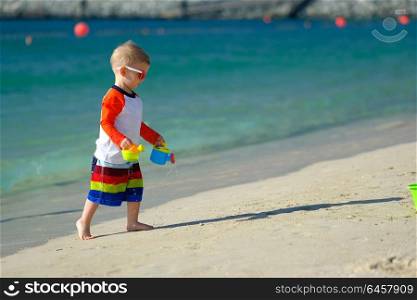 Two year old toddler boy playing with beach toys on beach