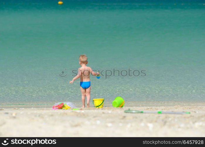 Two year old toddler boy playing with beach toys on beach