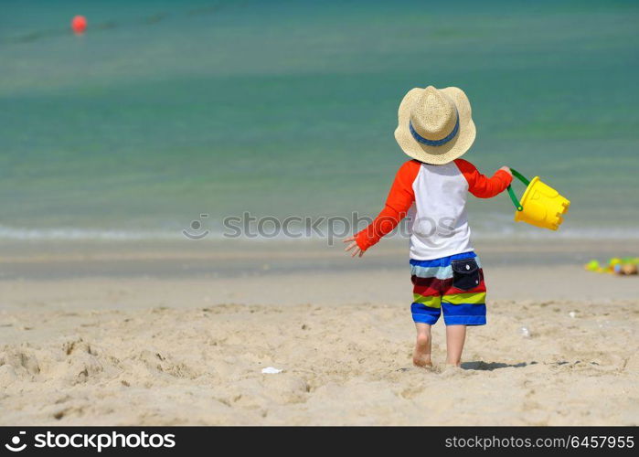 Two year old toddler boy playing with beach toys on beach