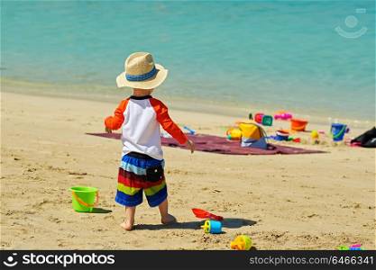 Two year old toddler boy playing with beach toys on beach