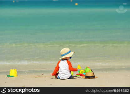 Two year old toddler boy playing with beach toys on beach