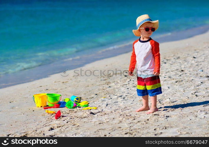 Two year old toddler boy playing with beach toys on beach