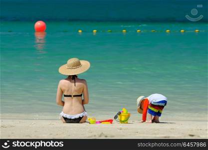 Two year old toddler boy playing with beach toys with mother on beach
