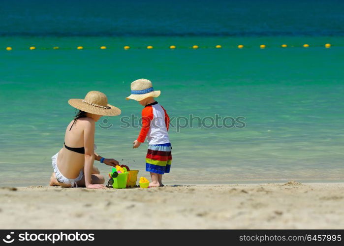 Two year old toddler boy playing with beach toys with mother on beach