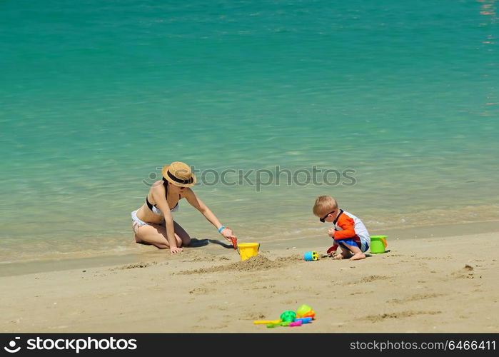 Two year old toddler boy playing with beach toys with mother on beach