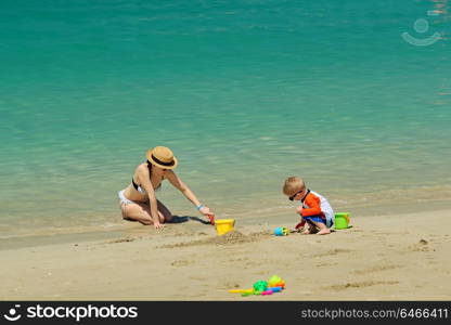 Two year old toddler boy playing with beach toys with mother on beach