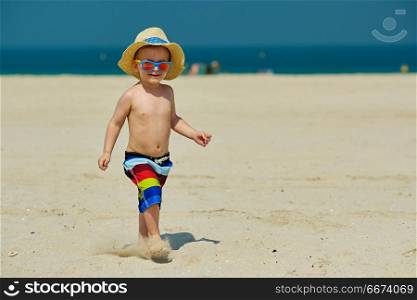 Two year old toddler boy running on beach . Two year old toddler boy in sun hat running on beach