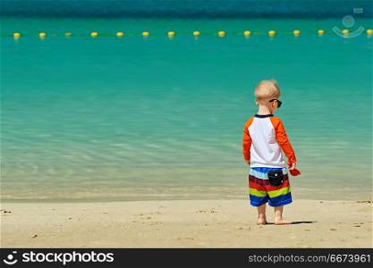 Two year old toddler boy walking on beach . Two year old toddler boy in sunglasses walking on beach