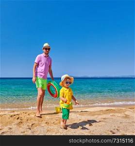 Two year old toddler boy walking on beach with father, holding inflatable ring. Summer family vacation. Sithonia, Greece. 