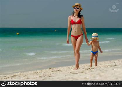 Two year old toddler boy walking on beach with mother