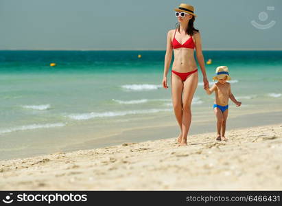 Two year old toddler boy walking on beach with mother