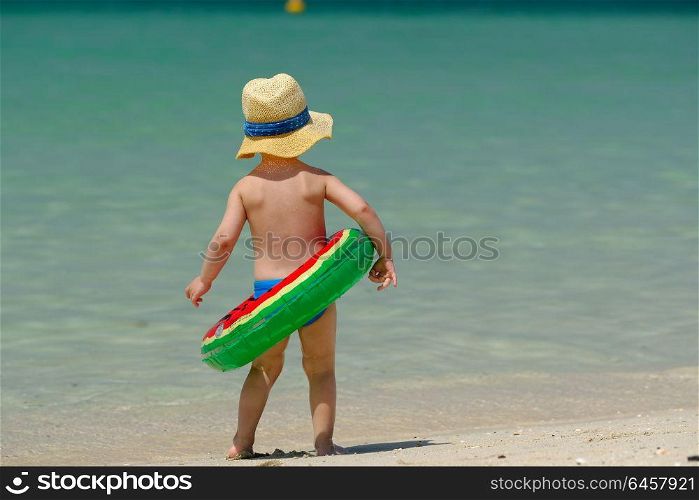 Two year old toddler boy with inflatable swim ring on beach
