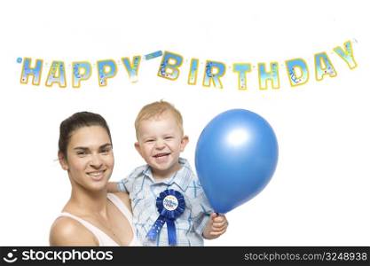 Two years old baby boy and mother together in front of a Happy Birthday sign.