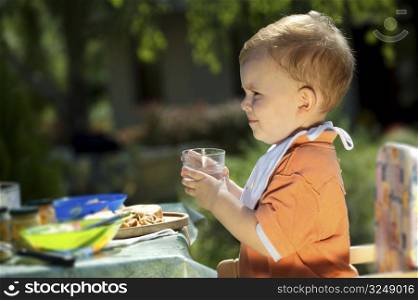 Two years old baby boy drinking. Family BBQ party outdoor, in the garden.