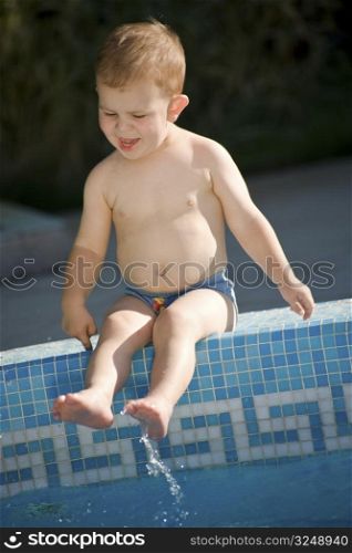 Two years old baby boy enjoys water and sunshine on the poolside. Natural light, summer.